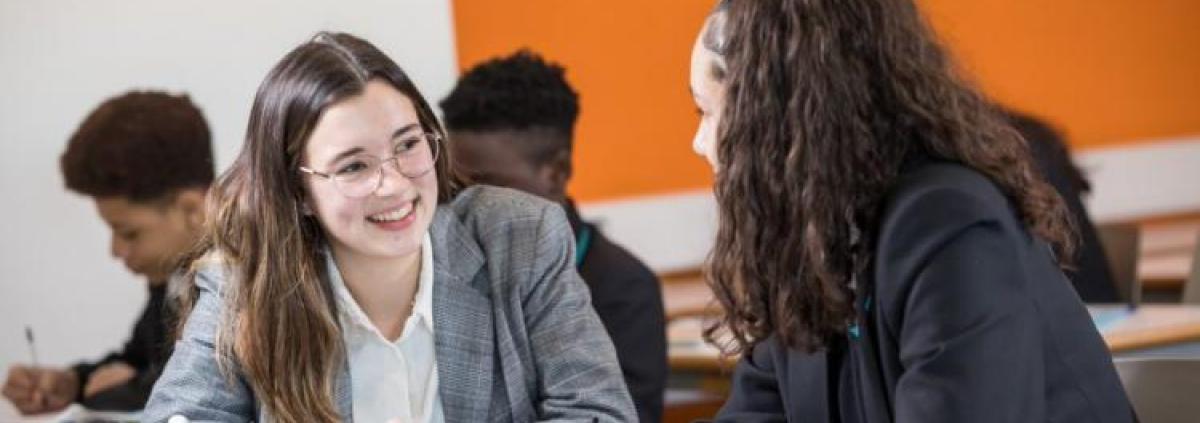 A teacher sat at a desk explaining a task to a student.