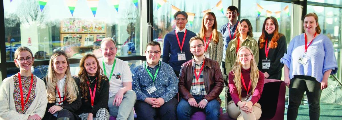 A group of young people, looking at the camera, smiling in the sunshine from a window